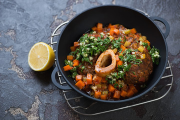Cast-iron pan with ossobuco made of cross cut veal shank and served with gremolata, studio shot