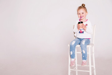 little girl is sitting on a chair and drinking from a coffee cup © ribalka yuli