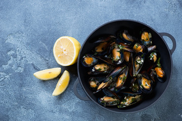 Above view of a cast-iron pan with freshly cooked mussels, blue stone background with copyspace, horizontal shot