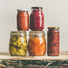 Autumn seasonal pickled or fermented colorful vegetables in glass jars over vintage kitchen drawer, white wall background, copy space, square crop. Fall home food preserving or canning