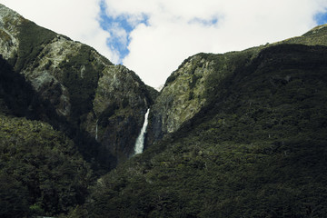 Imagen de una cascada cayendo con fuerza por una montaña bajo un cielo nuboso.