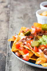 Mexican nachos with beef, guacamole, cheese sauce, peppers, tomato and onion in plate on wooden table