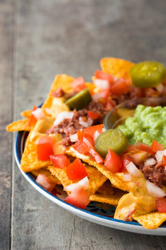 Mexican nachos with beef, guacamole, cheese sauce, peppers, tomato and onion in plate on wooden table
