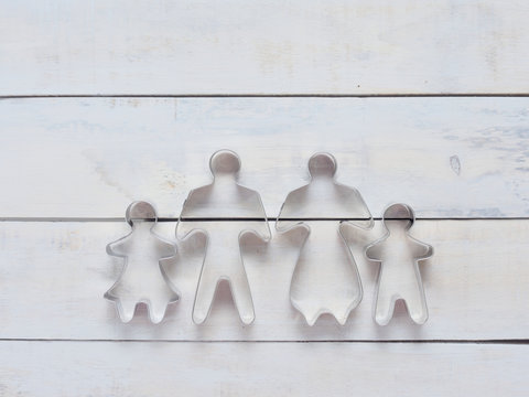 Family metal cookie or biscuit cutter used to cut dough in particular shape composed of father, mother, brother, and sister over rough white wooden background or surface