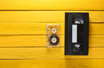 Vhs video cassette and audio cassette on a yellow wooden background. Retro media technology from the 80s. Top view.