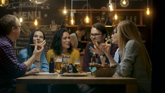 In the Bar/ Restaurant Group of Diverse Young People Eat Slices of Pizza Pie. They Talk, Tell Jokes and Have Fun in This Stylish Establishment. Shot on RED EPIC-W 8K Helium Cinema Camera.