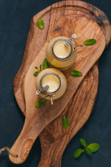 The yellow fruit smoothie in the glass bottles with straw on the wooden decorative cutting boards on the black table. View from above