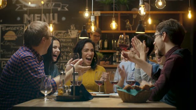 Diverse Group of Friends Celebrate with a Toast and Raise Wine Glasses in Celebration. Beautiful Young People Have Fun in the Stylish Bar/ Restaurant. Shot on RED EPIC-W 8K Helium Cinema Camera.