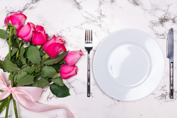 Decorated table setting for Valentine's Day with plate, fork, knife and bouquet of roses. Flat lay, top view.