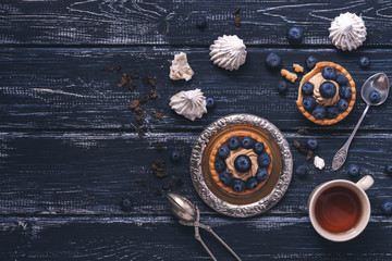 A capcake with cream and blueberries is served on a vintage metal saucer on a wooden background. Horizontal projection