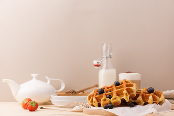 Tasty sweet waffles with berries and cup of cocoa with milk on beige background.