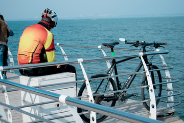a young man sits on the pier and looks at the sea, next to him lies a bicycle. Cyclist resting on the dock