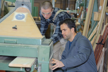 carpenter training male apprentice to use mechanized saw