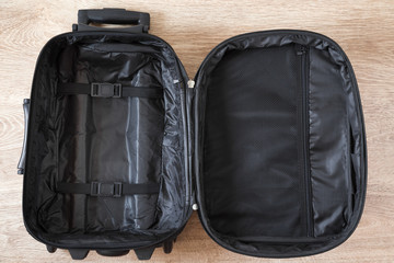 Opened empty, black travel bag for different things on the wooden floor. Travel preparation concept. 