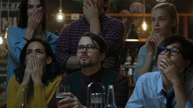 Young People in the Bar Watch TV Suddenly Breaking News Show that Tragic Events Unfold. Young People Are Horrified, Saddened and Shocked. Shot on RED EPIC-W 8K Helium Cinema Camera.
