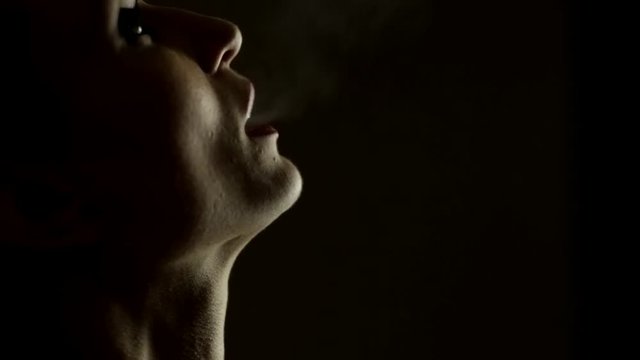 Silhouette of woman smoking on black. Slow motion