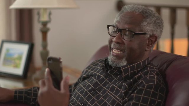 A happy elderly African American grandpa smiling talking on a smartphone or iPhone. Authentic family feel. Social distancing. Slow motion (48fps) Prores file.