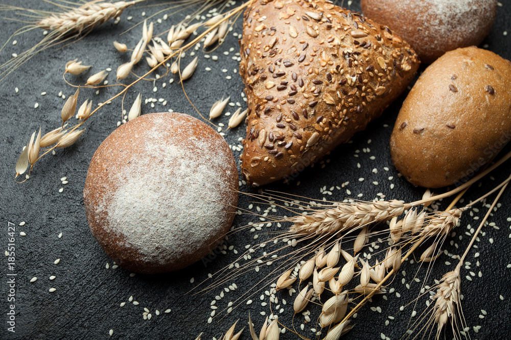Aufkleber fresh rustic bread with grains on a black table with spikelets of wheat and oats.