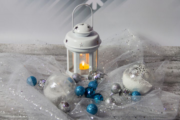 White metal lantern with candles surrounded by silver and blue shiny small Christmas balls on a...