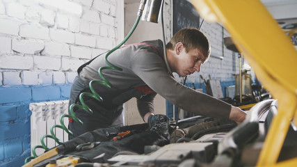 Mechanic in car repairing service - diagnostics in engine compartment