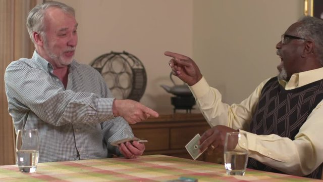 Two diverse elderly interracial friends, African American and Caucasian, laugh and have fun playing cards together. Slow motion (48fps) Prores file.