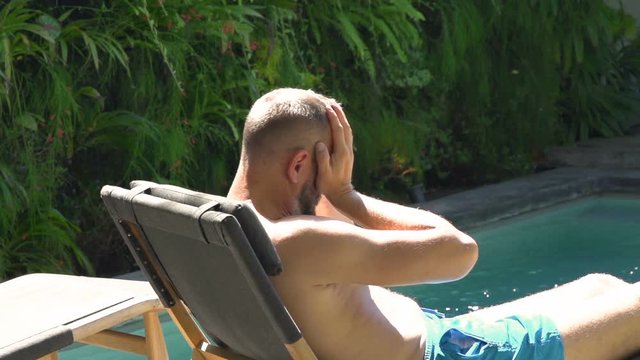 Man lying on sunbed next to the pool and looks worried, steadycam shot, slow motion shot at 240fps
