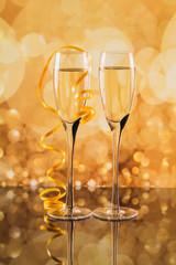 Two glasses of champagne with golden light bokeh on background.
