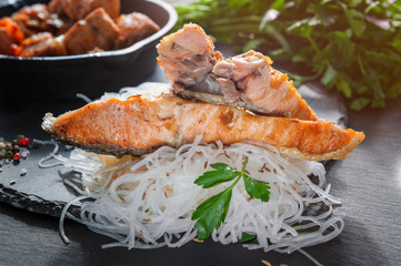 cellophane with pieces of roasted salmon with tomatoes, onion and parsley on the Board of black slate