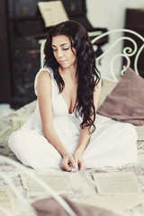 Portrait of beautiful woman, sitting on white bed with blurred piano on background