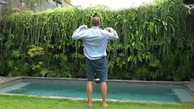 Man standing next to the pool and puts shirt on, steadycam shot, slow motion shot at 240fps
