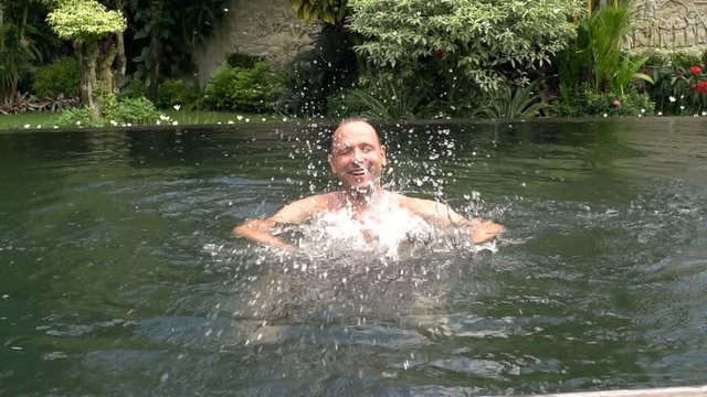 Happy man waving to the camera while relaxing in the pool, steadycam shot, slow motion shot at 240fps
