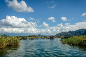 A hut on the end of a wooden pier in a distance on a lake with g