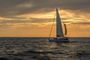 Naklejka na ściany i meble Sailboat on open sea during sunset under cloudy skies