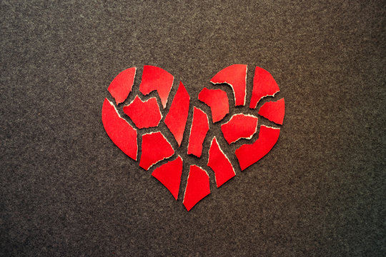Paper red broken heart on dark felt background. Mosaic paper heart from pieces. Cracked heart symbol. Broken love concept.