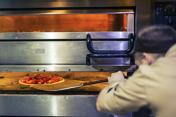 young chef at the restaurant prepares pizza