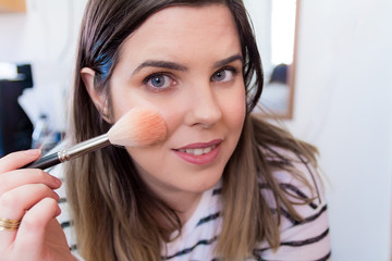 Woman applying makeup in her bedroom