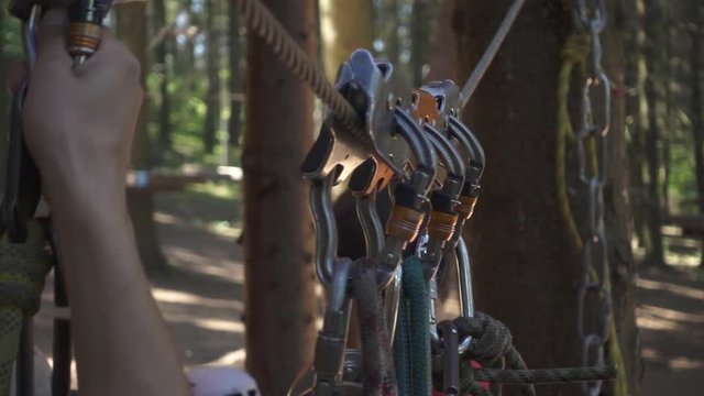 Male hand taking carabiner with ropes for extreme climbing trees in adventure park. Close up safety rope and carabiner for mountaineer in climbing park
