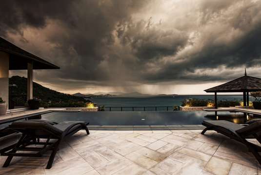 Storm coming up and dark clouds above Swimming pool with sea view in luxury villa, weather and rainy season