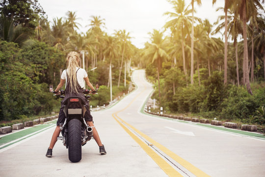 Portrait of female Biker sitting on big motorcycle. Girl driver with dread locks, travel way concept