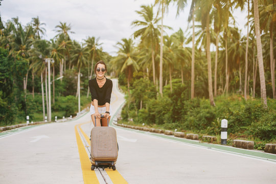 Beautiful style girl walking with suitcase on tropical road