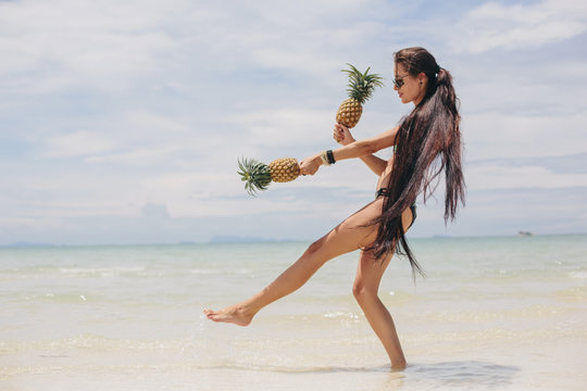 Beautiful happy female with very long hair holding pineapples on sea shore