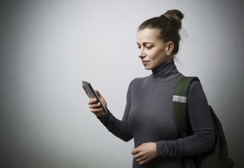Naklejka premium Attractive woman with a backpack looking into a smartphone. The girl is calling on the phone.