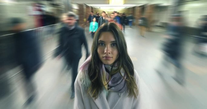 Beautiful young woman standing in moving crowd, looking at camera. 4K timelapse.