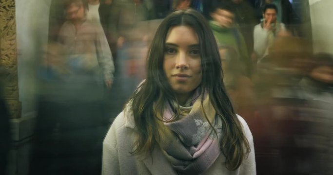 Beautiful young woman standing in moving crowd in subway, looking at camera
