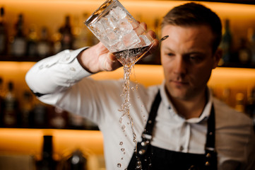 Young barman pouring water from a glass with ice cubes