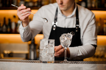 Barman holding a long spoon and glass with ice cubes