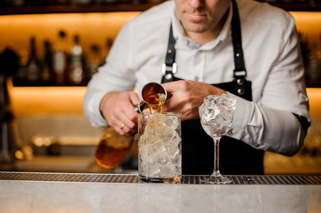 Barman adding alcoholic drink into a glass filled with ice cubes