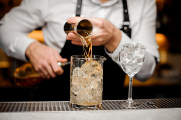 Barman pouring alcoholic drink into a large glass filled with ice cubes