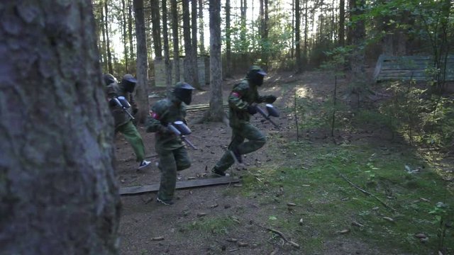 Paintball player running on battle field during shooting game in summer forest slow motion. Team players with gun playing in paintball game in adventure park