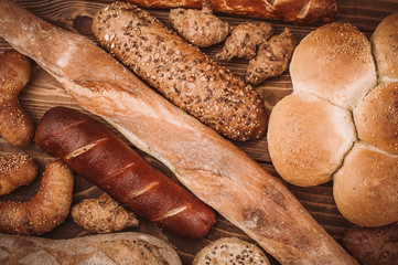 Many mixed baked breads and rolls on rustic wooden table
